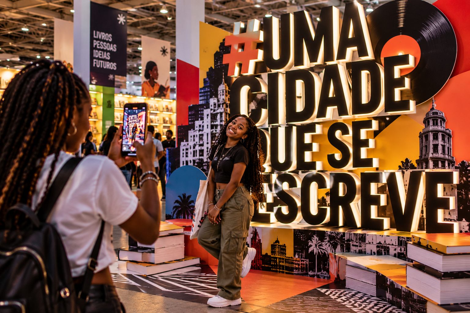 Jovem posa para uma fotografia em frente ao letreiro #UmaCidadeQueSeEscreve